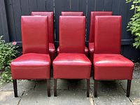Six red faux leather dining chairs arranged in two rows of three in outdoor patio setting, showing front view with visible minor wear and some creasing on seats and backs.