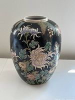 Front view of the black ceramic vase showing intricate raised floral patterns in pastel colors against the dark background.