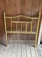 Front view of one single brass headboard showing vertical brass rods with rounded finials and slight wear.