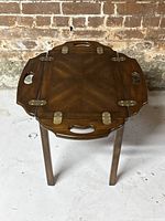 Top angled view of wooden butler table showing folding sides partially extended and brass hinges. Visible minor wear marks on the tabletop.