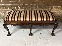 Front view of the antique mahogany bench with silk upholstery and carved legs and apron.