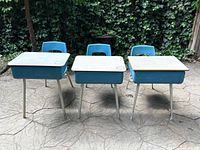 Front view of three vintage school desks with attached blue plastic chairs, showing different angles of desk tops and support legs.