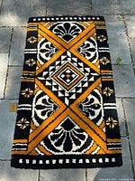 Full view of the rectangular rug showing the overall black, orange and white bold pattern design from a top-down angle on a stone surface.