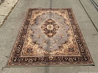 Full view of the Persian style wool rug laid flat on concrete showing central medallion and border designs with overall condition and some stains.
