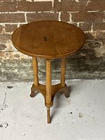 Side view of the vintage round pine side table showing turned legs and stretcher base.