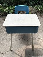 Front view of blue vintage school desk with pale cream laminate desktop and blue metal body and beige metal legs.