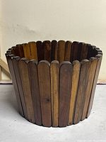 Front angle view of the round waste paper bucket showing vertical wood slats and scalloped top edge.