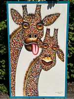 Full view of large acrylic canvas painting depicting two colorful giraffes, one with tongue sticking out, signed by Adi Saputra