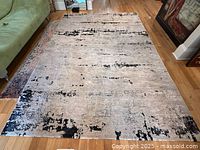 Modern white and black area rug measuring 90x130 inches, placed on wooden floor with light wear and one visible small stain on the surface.