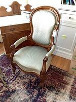 Front view of antique wooden upholstered chair showing curved backrest and armrests