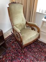 Front angle view of the antique rocking chair showing the upholstered striped fabric and wooden frame with carved armrests and backrest detail.