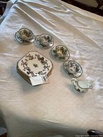Set displayed on white cloth: 4 cups, 8 snack plates, 1 creamer with floral and gold trim.