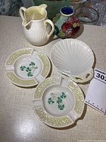Five items shown: two Belleek shamrock ashtrays, white ribbed pitcher, shell-shaped dish, and small Moorcroft vase.