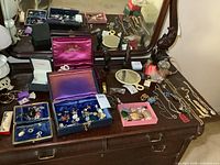 Full overview of the dresser with multiple boxes of jewelry, necklaces, figures, mirrors and other assorted costume jewelry items