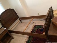 View of the vintage solid walnut single bed frame showing the side rails, headboard, and footboard assembled in a room on carpet.