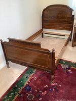 Full view of the assembled vintage solid walnut single bed frame showing the headboard, footboard, and side rails positioned on carpeted floor.