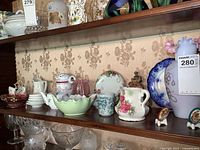 Overall view of glass and china items on wooden shelf including vase, plates, pitchers, small dishes, and teapots
