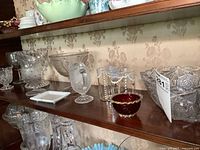 Overview photo showing entire shelf with assorted glassware including pitchers, pedestal bowls, compote bowl, and small red bowl