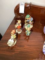 Four Goebel Hummel porcelain figurines arranged on wooden surface showing various characters.