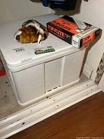 White plastic cabinet with a plush tiger headcover and Top-Flite golf ball box on top