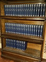 Full view of 52 Harvard Classics volumes arranged on wooden shelves in three rows, showing the uniform dark blue hardcover spines with gold lettering and shield logo.