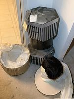 Two black and gray striped hat boxes stacked, one open with tissue paper inside, a striped hat, and a short black wig on a mannequin head.