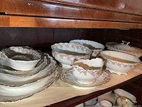 Photo of multiple Limoges porcelain serving dishes and bowls arranged on shelf showing floral pink pattern and gold trim.