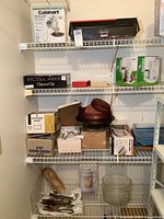 Shelves with boxed kitchen appliances, bowls, and cutlery set. Includes Cuisinart mixer box at top left and various glass and wooden kitchenware items.