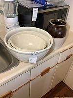 Set of three nesting stoneware mixing bowls on counter with a blender, microwave, and stoneware churn nearby.