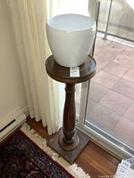 Full view of antique wooden plant stand with modern white planter on top, near window.