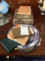 Photo of two decorative plates stacked showing their intricate floral and geometric designs with gold trim, with boxed sets of cutlery arranged on top.