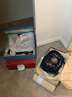 Photo of several ladies purses in their boxes with tissue paper, showing a blue purse with floral embroidery.