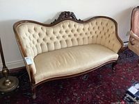 Front and side angled view of the antique wooden frame settee with beige tufted upholstery and carved floral detail on backrest.