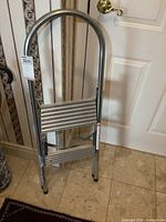 Small folding metal step ladder folded upright against a door on tile floor.