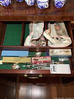 Top view of open drawer showing spoons, salad tongs, and boxed sugar spoons with cloth liners in adjacent compartments.