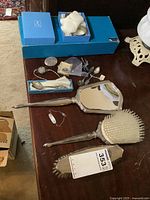 Overview of lot with blue box containing napkin rings, various spoons, pocket watch, brooches, ID bracelet, vanity mirror, hairbrush, clothes brush
