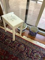 Painted wood side table and two porcelain planters placed on a floor near a glass door, shows floral design on the table top and details of the two porcelain planters