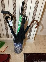 Porcelain umbrella holder showing several umbrellas and a black cane inside.