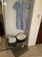 Blue and white striped vintage nursing dress hanging on hanger on wall, showing full length and pleated front