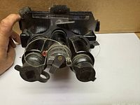 Front underside view showing objective lenses, lens caps, battery cap, mounting bracket