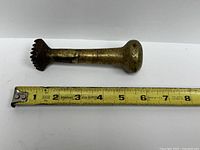 brass pestle beside measuring tape showing length