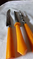 Set of three carving utensils on a fabric surface, showing profiles of butterscotch Bakelite handles and steel parts.