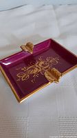 Close-up of deep purple rectangular ashtray with gold gilded leaf holders and floral design.