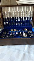 Open wood presentation box with 12 knives upright and mixed forks and spoons below