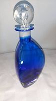 Image showing front of blue glass decanter with clear spherical stopper featuring etched design.