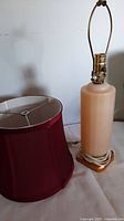 Vintage pale pink glass Art Deco style table lamp with brass socket and gilded foot, lamp positioned next to a burgundy fabric lampshade.