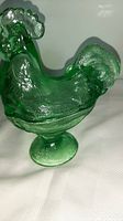 Green translucent glass hen figurine with textured feathers and comb, standing on a pedestal base shaped like a nest with leaf patterns.