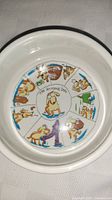 Top inside view of the dog bowl showing segmented colorful cartoon illustrations of dogs engaging in various activities, centered around 'The 24 Hour Dog' text.