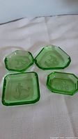 Four green depression glass dishes viewed from above, showing sporting intaglio designs.