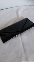Closed view of the black patent leather purse showing the glossy exterior and envelope style flap